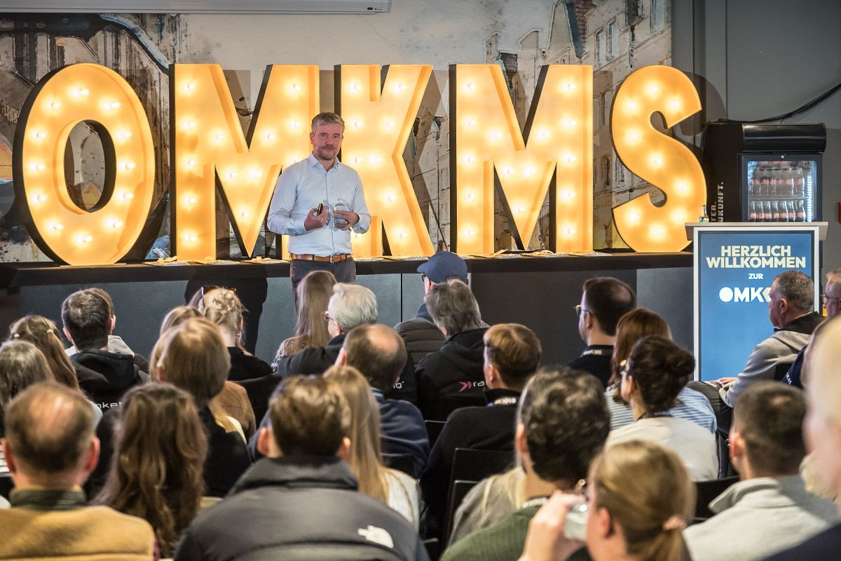 Keynote vor den leuchtenden OMKMS-Buchstaben